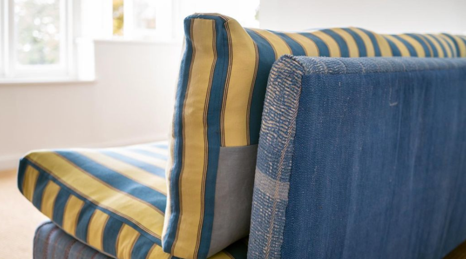 Blue sofa with stripy yellow and blue cushions facing a window.