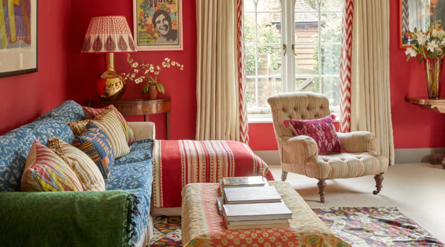 Bright and colourful room with red walls and a green and blue sofa. It has a cosy and comfortable style with bold lamps and a maximalist style.